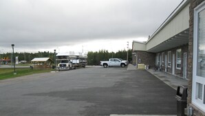 A parking lot with a building on the right and a truck in the distance. - Goodman's Motel (Baldwin)