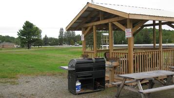 A wooden gazebo with a picnic table and a barbecue grill.