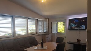 A living room with a sofa, a dining table, and a TV mounted on the wall. - Apartments Ivancevic (Korcula)