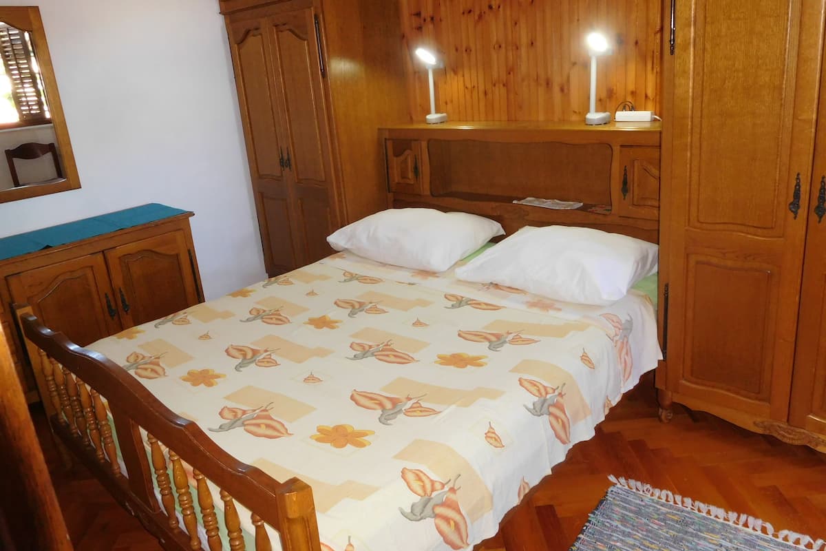 A bedroom with a bed, wooden wardrobe, and two bedside lamps.