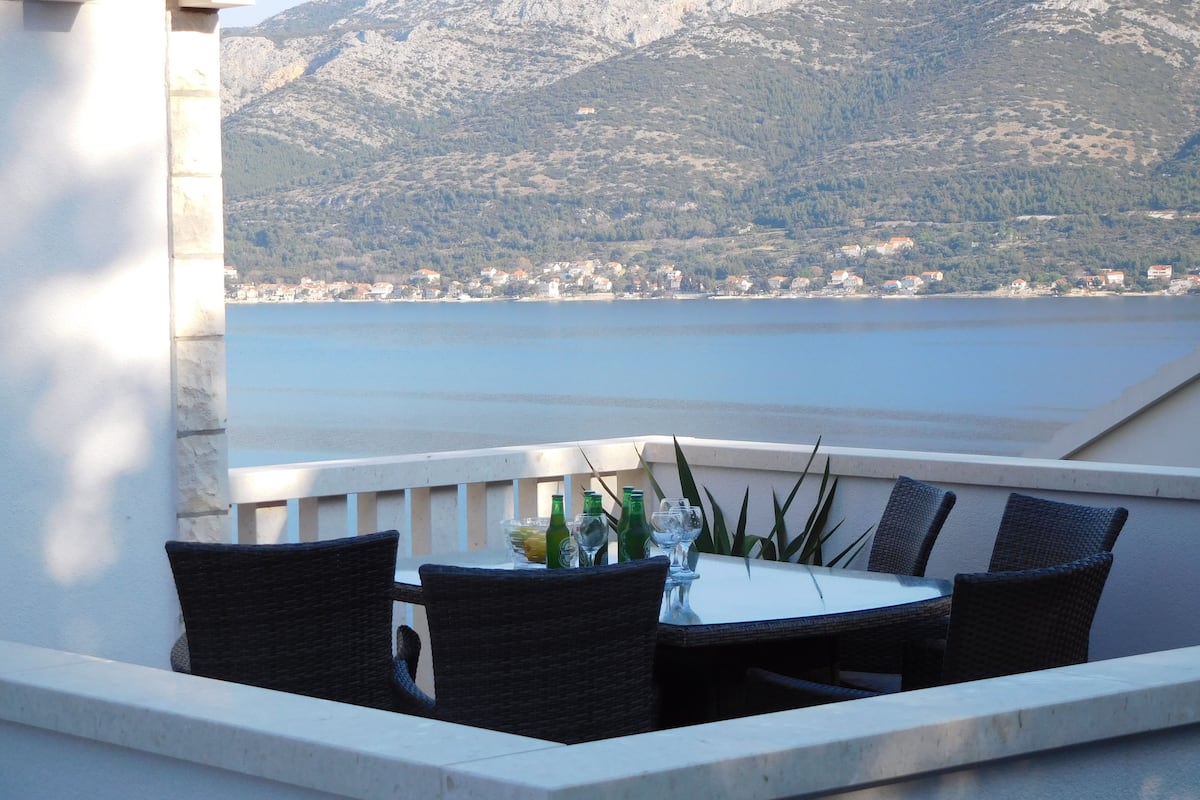 A terrace with a table and chairs, overlooking a lake and mountains.