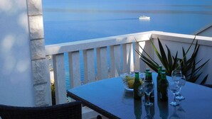 A table with bottles and glasses on a balcony overlooking a calm lake with a boat in the distance. - Apartments Ivancevic (Korcula)