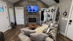 A living room with a stone fireplace, a television mounted on the wall, and a large mirror. - Soul Sister- Creek View, WiFi, Firepit, WiFi, Hiking, 4 mins to Natural Bridge (Campton)