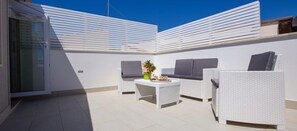 A rooftop patio with white wicker furniture, a small table with a plant, and a clear blue sky. - Aruci B&B (Syracuse)