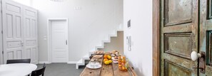 A hallway with a wooden table set with food, a staircase, and white doors. - Aruci B&B (Syracuse)