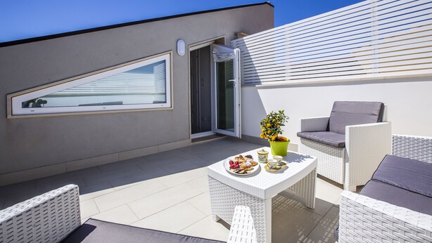 Un balcone con un divano in vimini bianco, un tavolino con dolci e una pianta in vaso.