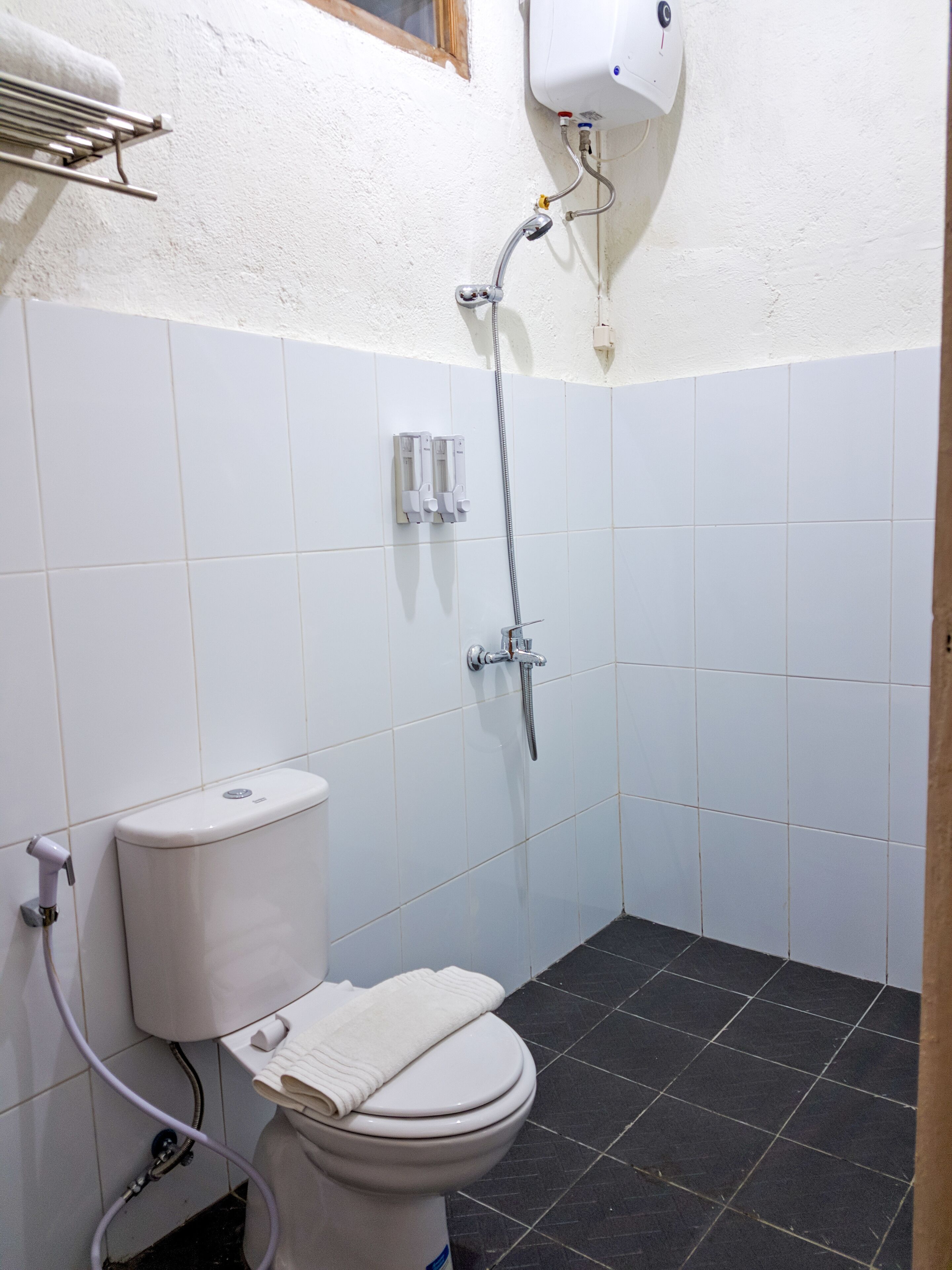A bathroom with a toilet, a shower, and a white wall with a window.