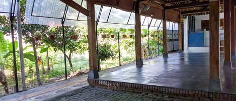 Un espace extérieur abrité, doté d’un sol en briques, de poutres en bois et offrant une vue sur une végétation luxuriante grâce à de grandes fenêtres.