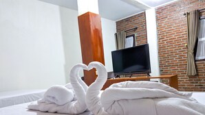 A hotel room with a bed, a TV, and a brick wall. - Griya Jagadhaya (Sewon)