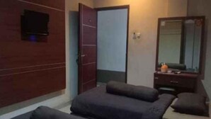 A room with two beds, a dresser, a mirror, and a television on the wall. - Happy Inn Hotel (Kendari)