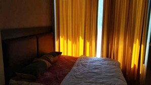 A bed with a headboard, a pillow, and a blanket in a room with curtains.
