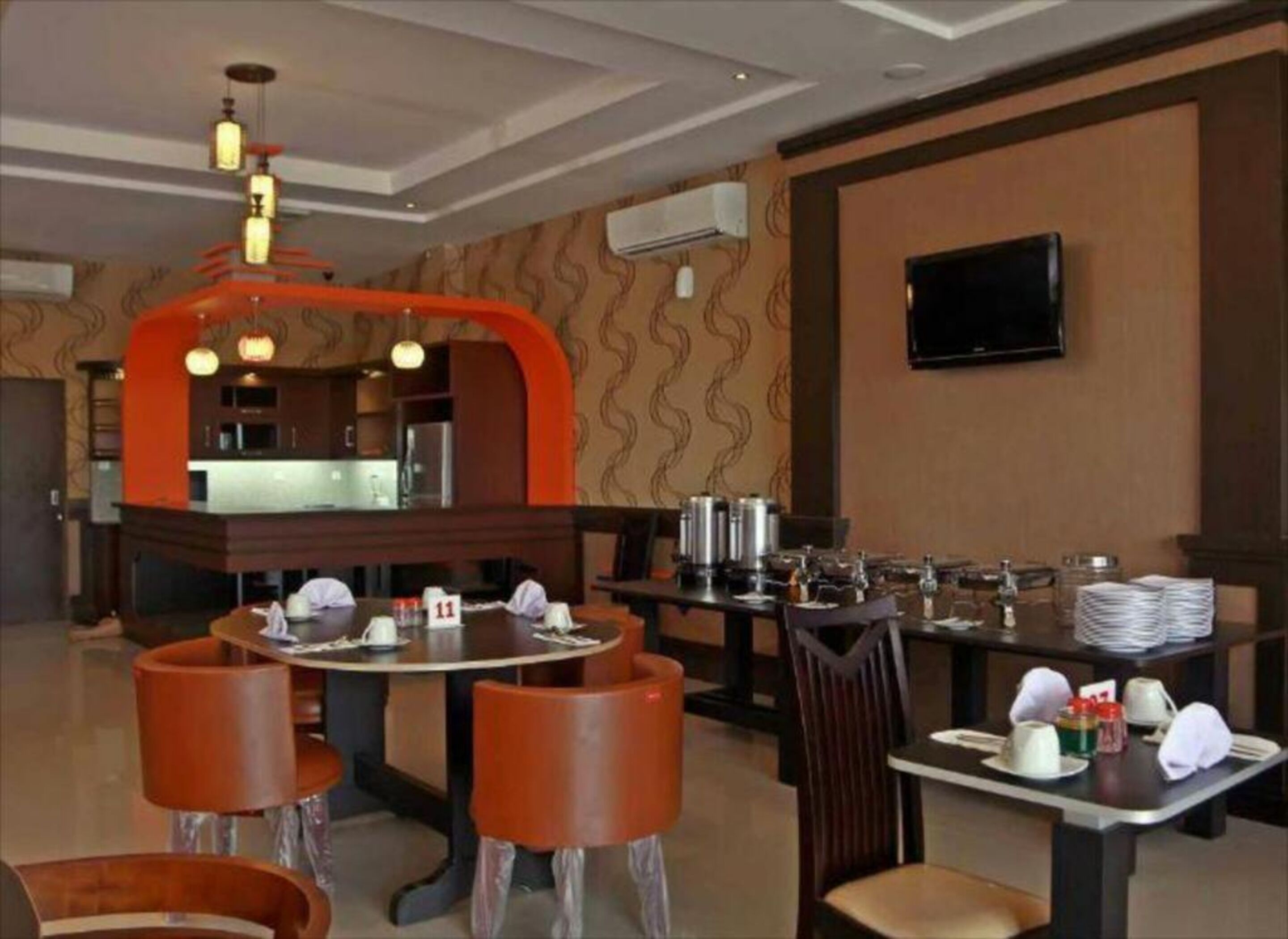 A restaurant with round tables, orange chairs, and a kitchen area in the background.