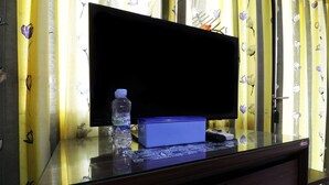 Habitación de hotel con un televisor de pantalla plana grande sobre una mesa de vidrio, una botella de agua y una caja azul.