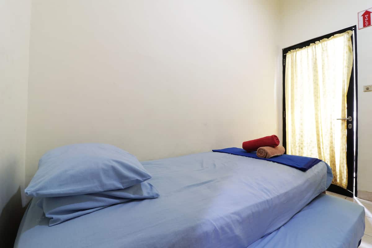 A single bed with blue bedding and pillows, a rolled towel, and a blue mat.
