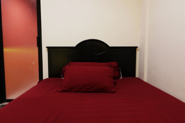 A single bed with a black headboard and red bedding in a room with white walls.