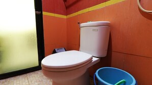 Un inodoro con asiento y tanque blancos, un cubo azul y un suelo de baldosas con una franja amarilla y roja.