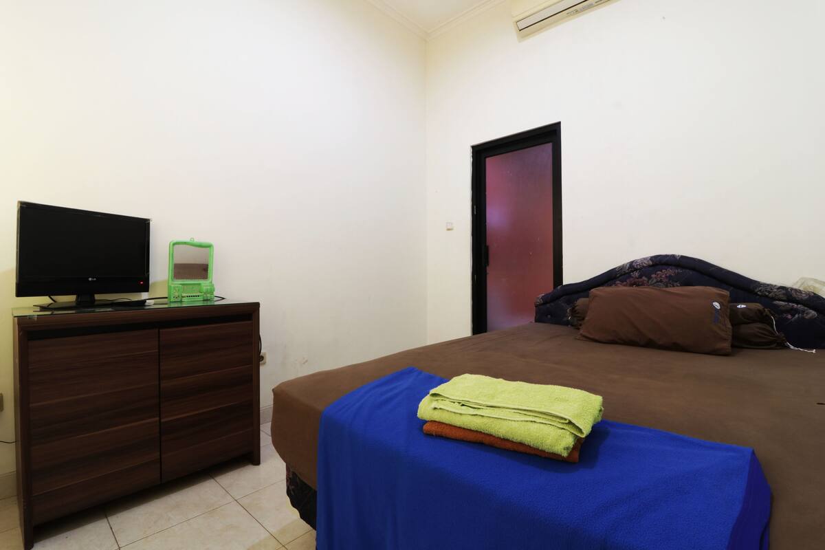 A bedroom with a bed, a TV on a dresser, and a door.