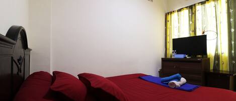 A room with a bed, a television on a stand, and a wardrobe.