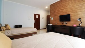 A hotel room with two beds, a wooden accent wall, a TV, a desk with a chair, and a lamp. - Wisma Konservasi (Jakarta)