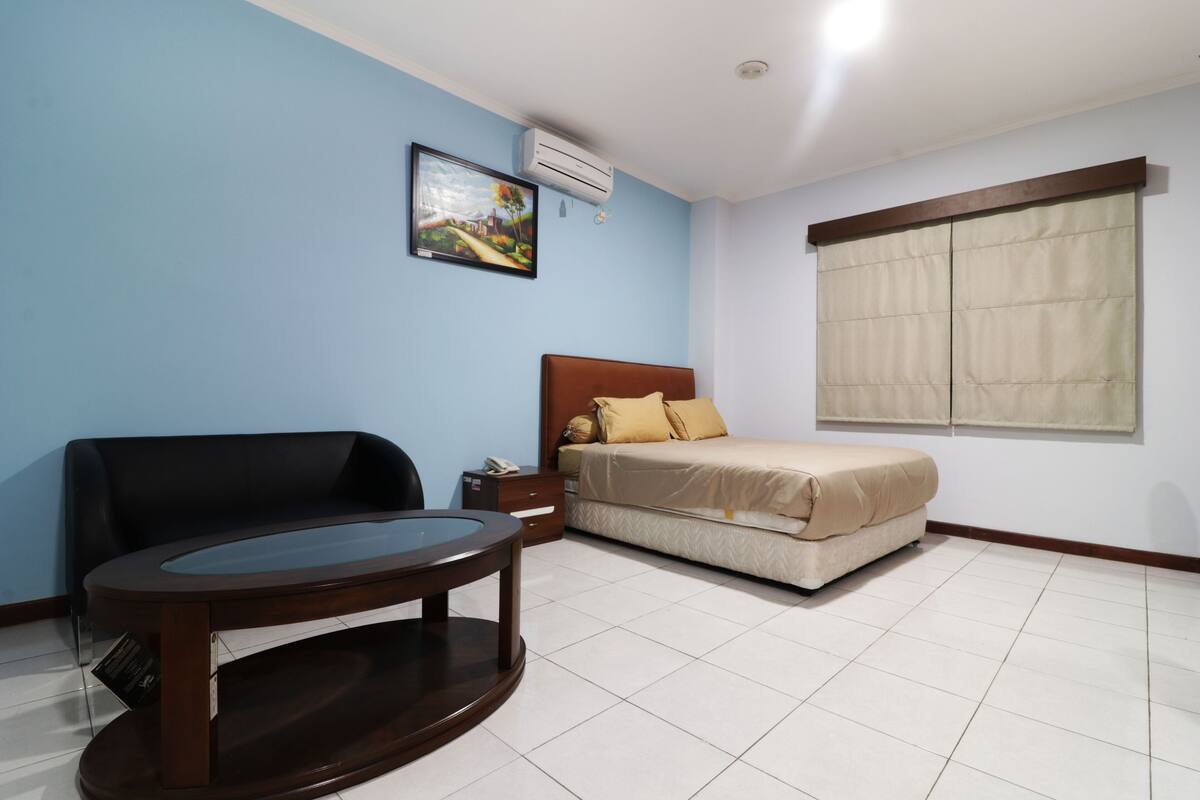 Un dormitorio con cama, sofá, una mesita y ventana con cortinas.