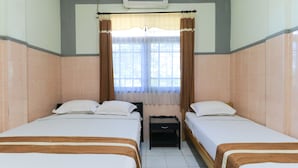 A hotel room with two beds, a window with curtains, a small table, and a ceiling-mounted air conditioner. - Wisma Flamboyan (Surabaya)