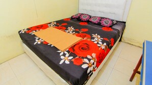 A bed with a floral bedspread and a brown blanket, a white headboard, and a blue wall. - Wisma TheBlossom (Padang)