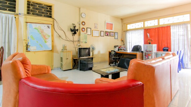 A living room with a red sofa, a television, a desk, and a map on the wall. - Wisma TheBlossom (Padang)