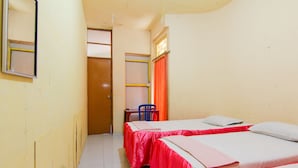 A narrow hallway leading to a room with two beds, a chair, and a window with orange curtains. - Wisma TheBlossom (Padang)