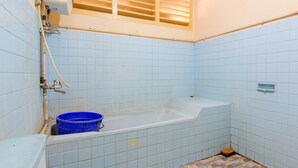 A bathroom with a bathtub, a blue bucket, and tiled walls. - Wisma TheBlossom (Padang)