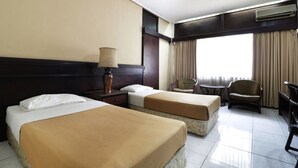 A hotel room with two beds, a chair, a small table, and an air conditioning unit. - Hotel Istana Bandung (Bandung)