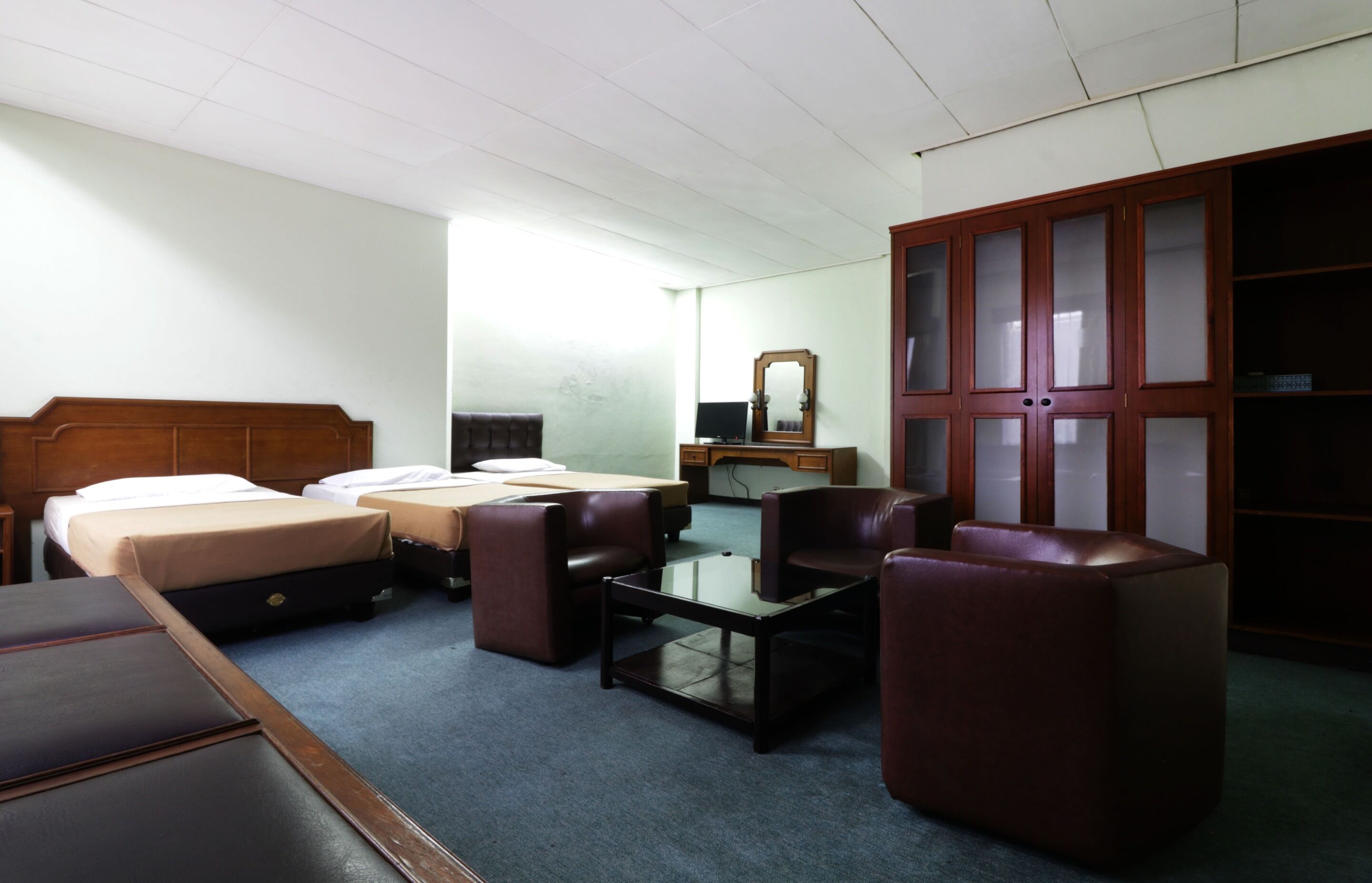 Ein Hotelzimmer mit zwei Betten, einem Schreibtisch, einem Stuhl, einem Kleiderschrank und einem Spiegel.