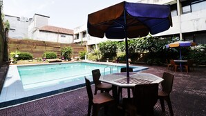 A swimming pool with a tiled deck, surrounded by a garden with various plants and a wooden fence. - Hotel Istana Bandung (Bandung)