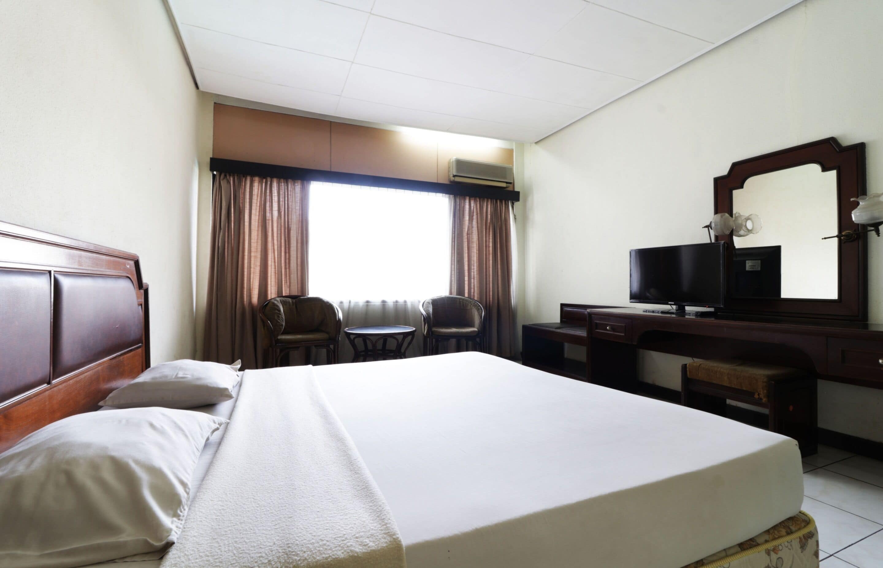 A hotel room with a large bed, a desk with a computer, a chair, and a window with curtains.