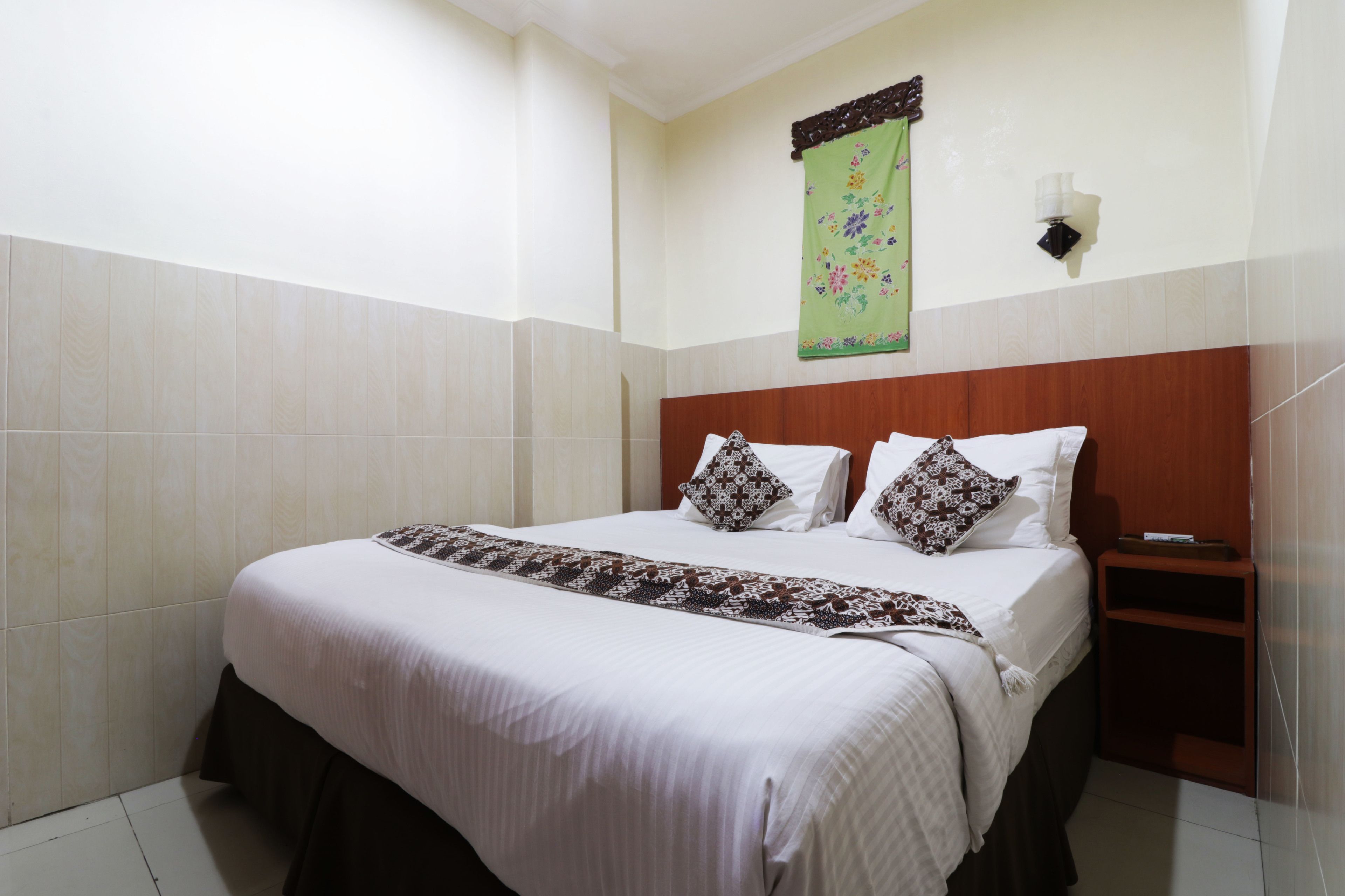 Ein Hotelzimmer mit einem großen Bett, einem hölzernen Kopfteil, einem Nachttisch und einem grünen Wandbild.