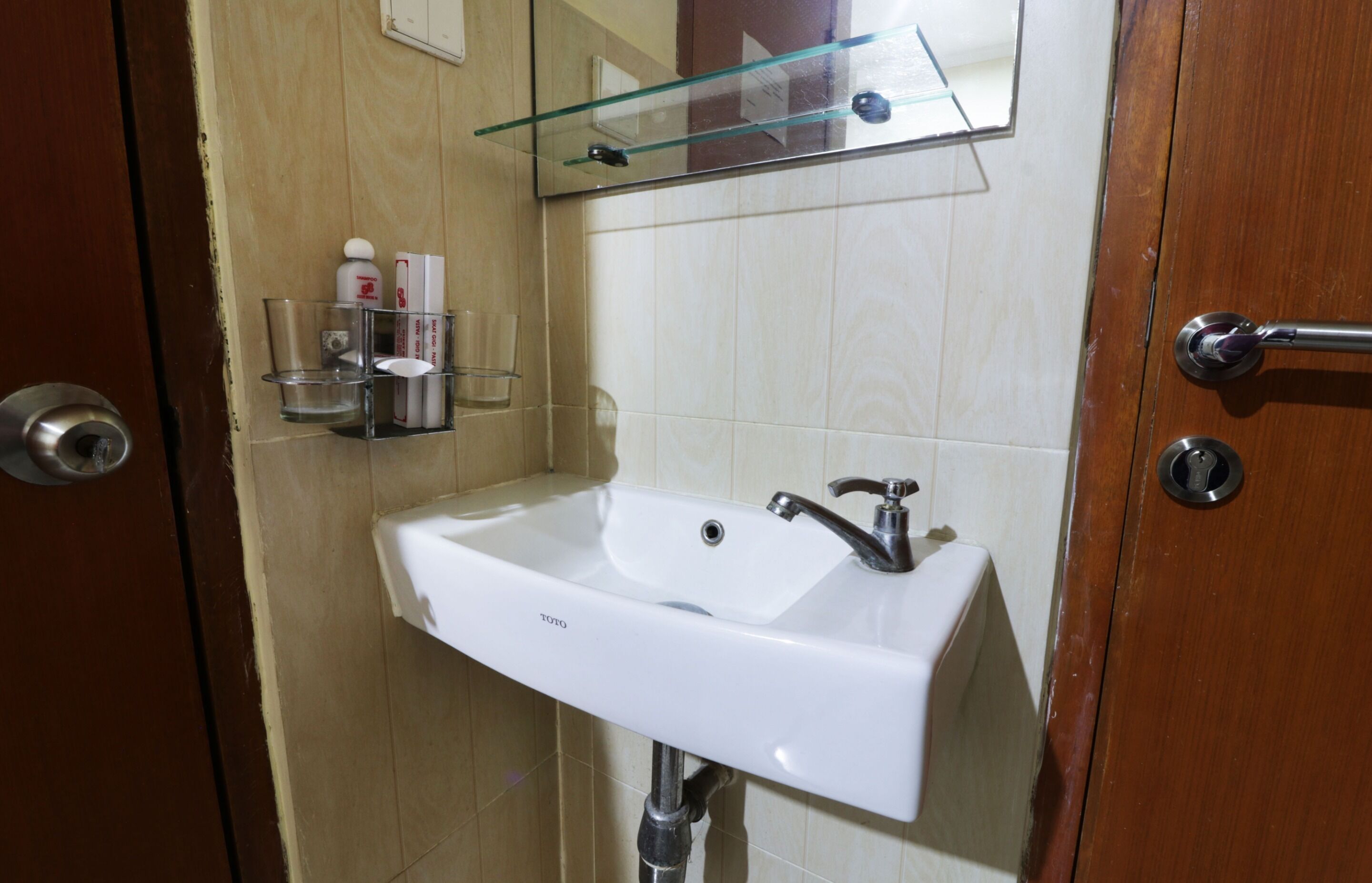 A bathroom with a white sink, a glass shelf with toiletries, and a mirror above the sink.