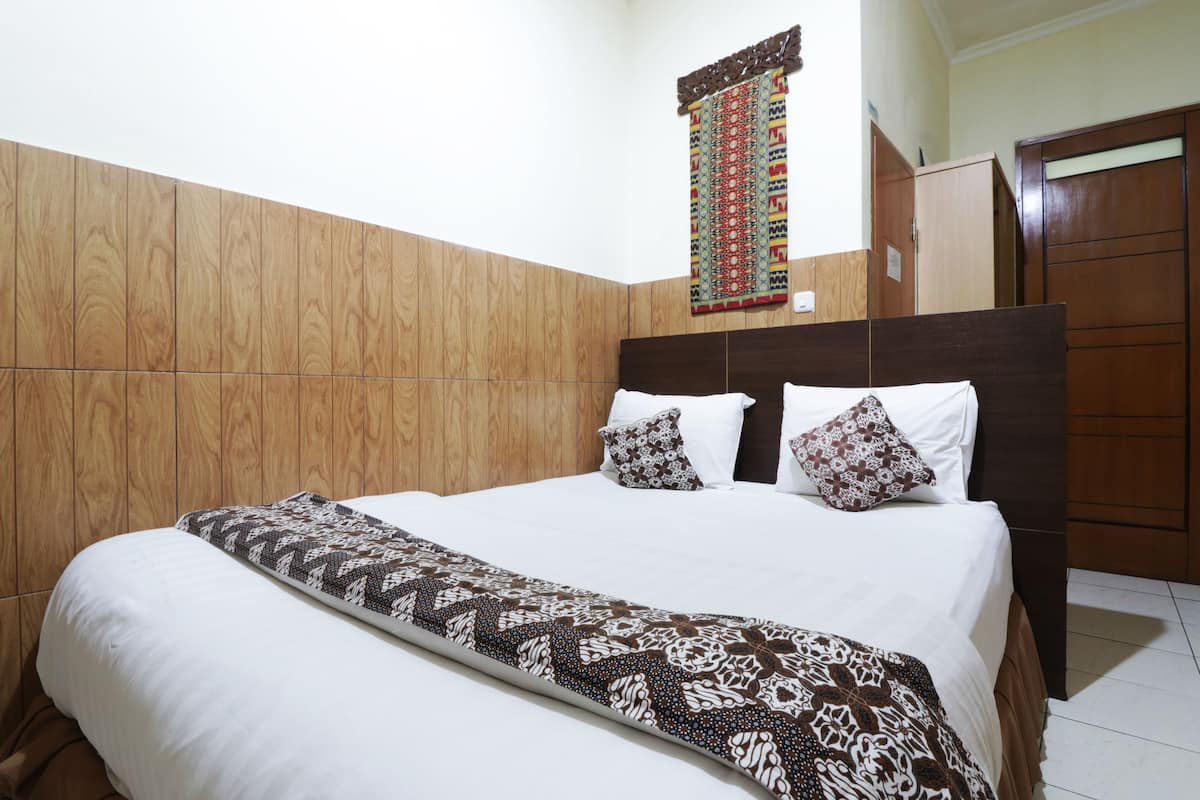 A neatly made bed with a patterned bedspread and pillows, a wooden headboard, and a wall hanging.
