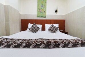 A hotel room with a large bed, two pillows, a wooden headboard, a green floral wall hanging, and a nightstand with a lamp. - 58 Guesthouse Tangerang (South Tangerang)