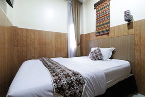 A neatly made bed with a patterned throw, wooden paneling on the walls, and a wall-mounted light fixture. - 58 Guesthouse Tangerang (South Tangerang)