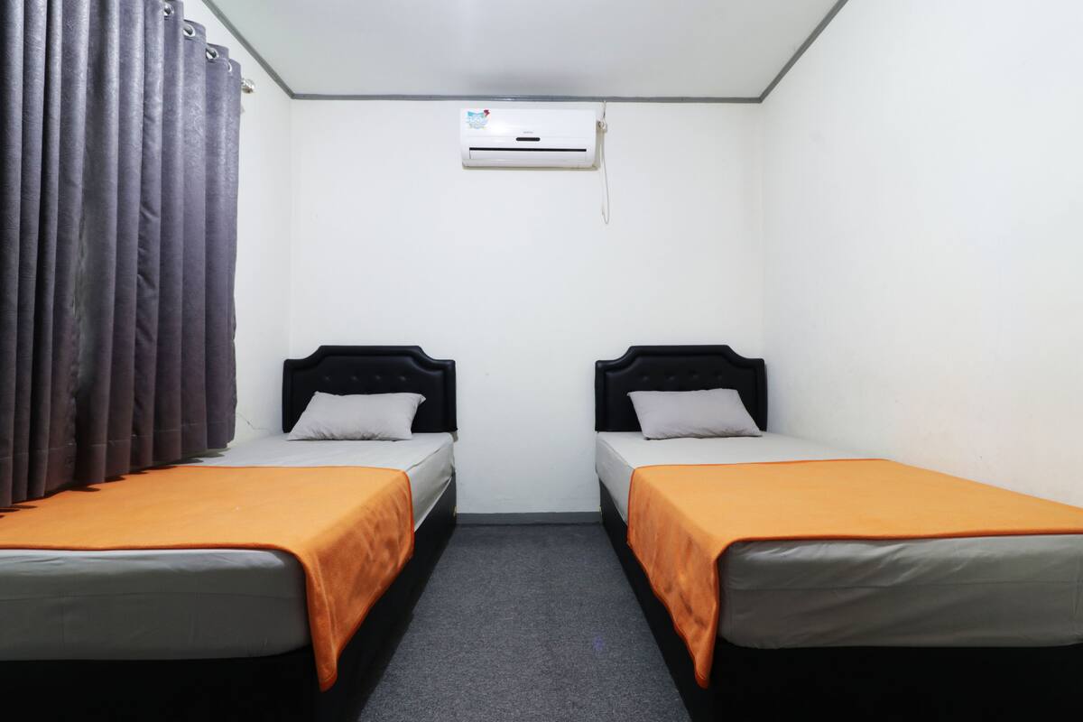 A room with two single beds, an air conditioning unit, and a curtain.