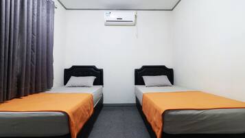 A room with two single beds, an air conditioning unit, and a curtain.