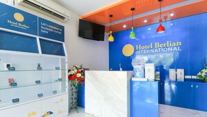 A reception area with a blue wall, a marble counter, and a glass display case with brochures. - Hotel Berlian International (Surabaya)
