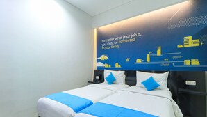 A hotel room with two beds, each with white bedding and blue accents, a large wall mural with text and cityscape graphics, and a nightstand with a phone and charger. - Hotel Berlian International (Surabaya)