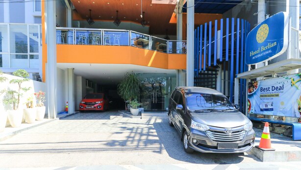 A hotel entrance with a car parked in front, a balcony with chairs, and a sign for Hotel Berlin International. - Hotel Berlian International (Surabaya)