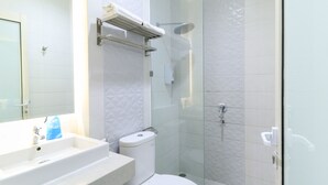 A modern bathroom with a white sink, toilet, and glass-enclosed shower. - Hotel Berlian International (Surabaya)