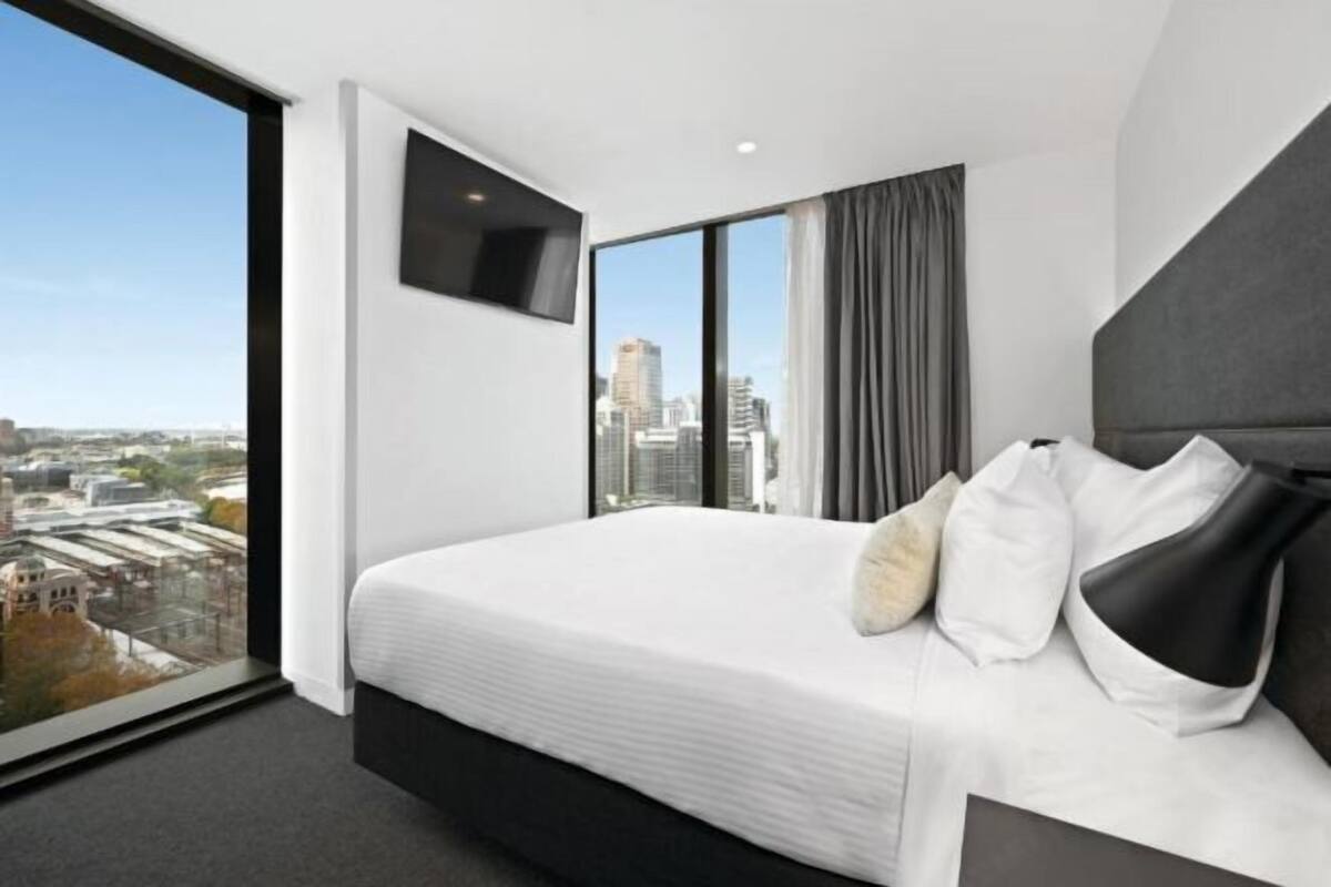 Ein modernes Hotelzimmer mit einem großen Bett, einem Flachbildfernseher, Blick auf die Stadt und einem großen Fenster.