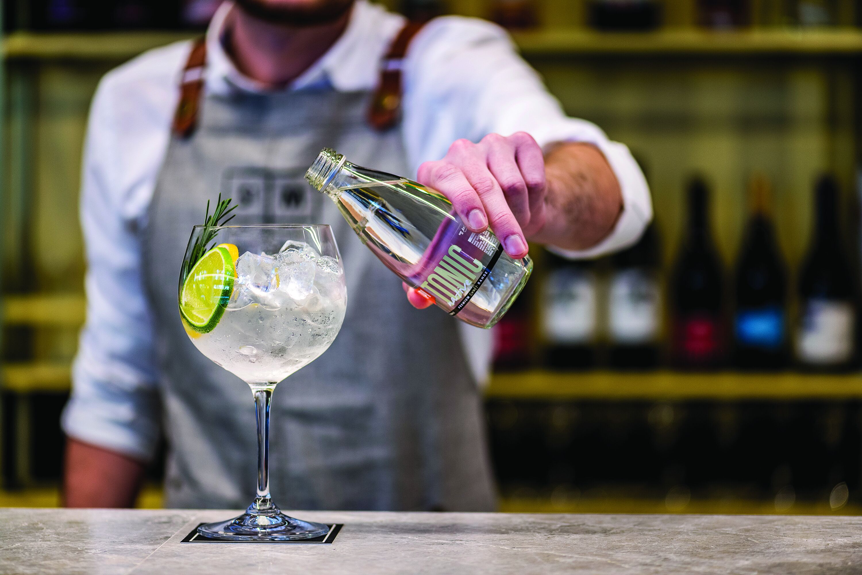 A bartender pouring a drink into a glass with ice and a lime slice.