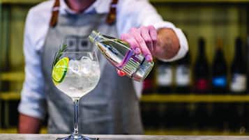 A bartender pouring a drink into a glass with ice and a lime slice.