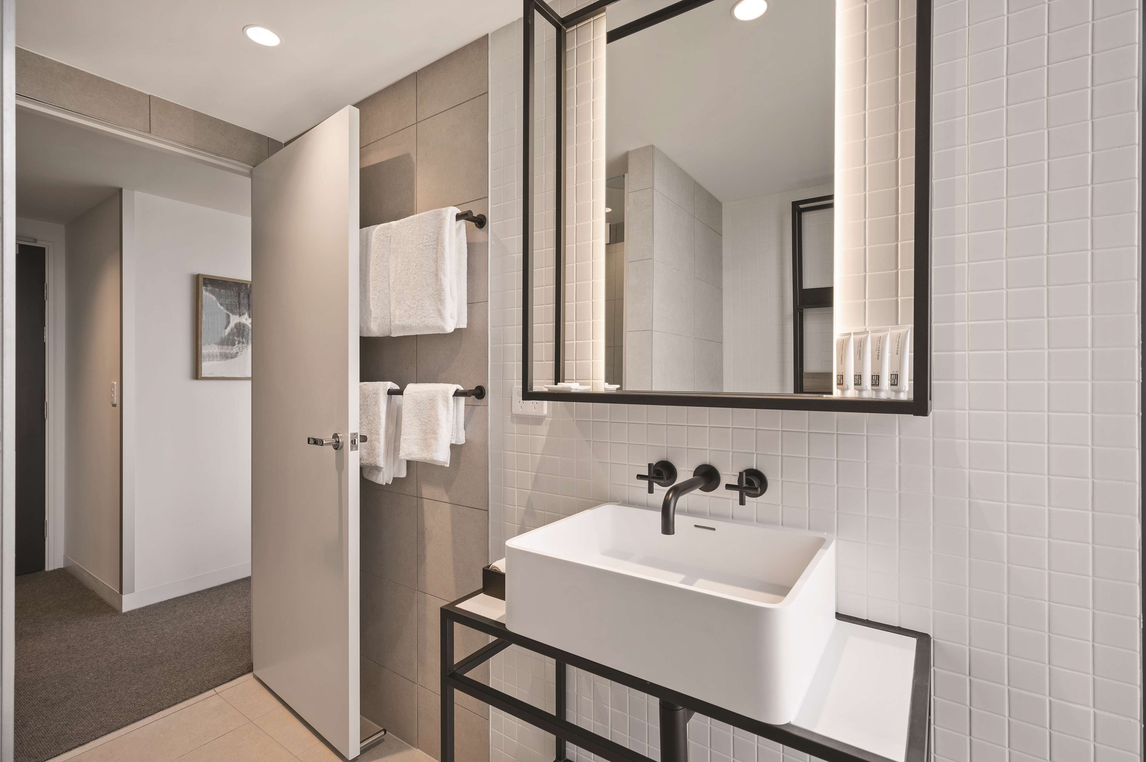 Un baño moderno con un lavamanos blanco, un espejo grande y una zona de ducha.