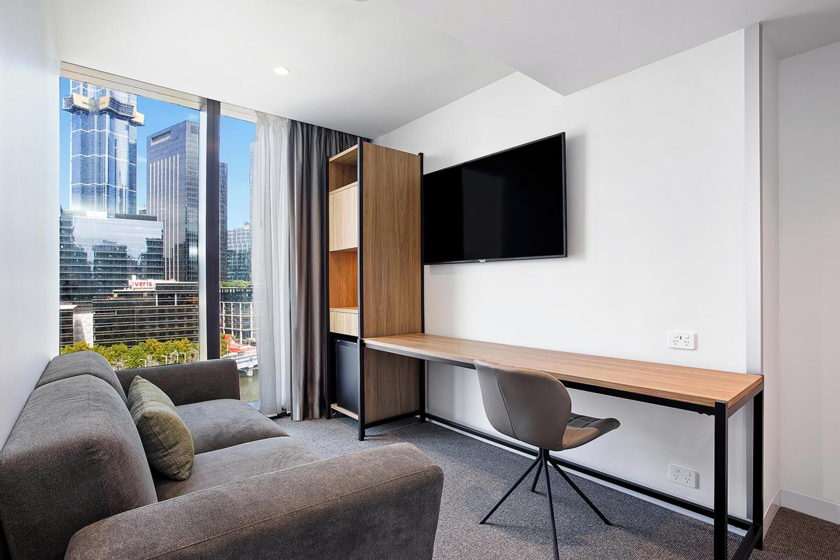 Una habitación de hotel moderna con un sofá, un escritorio y un televisor montado en la pared.