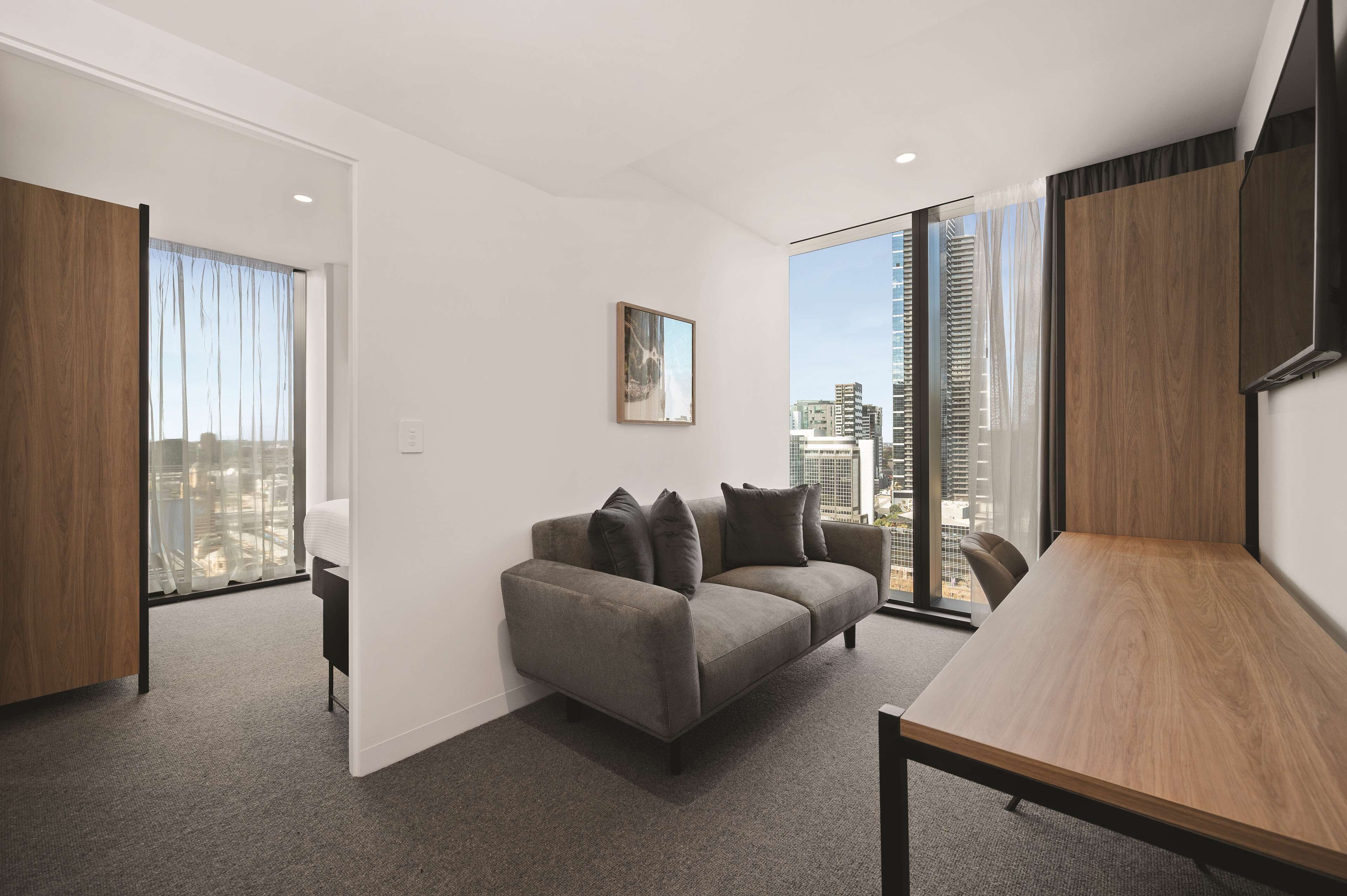 A modern living room with a grey sofa, a wooden coffee table, and a large window offering a city view.